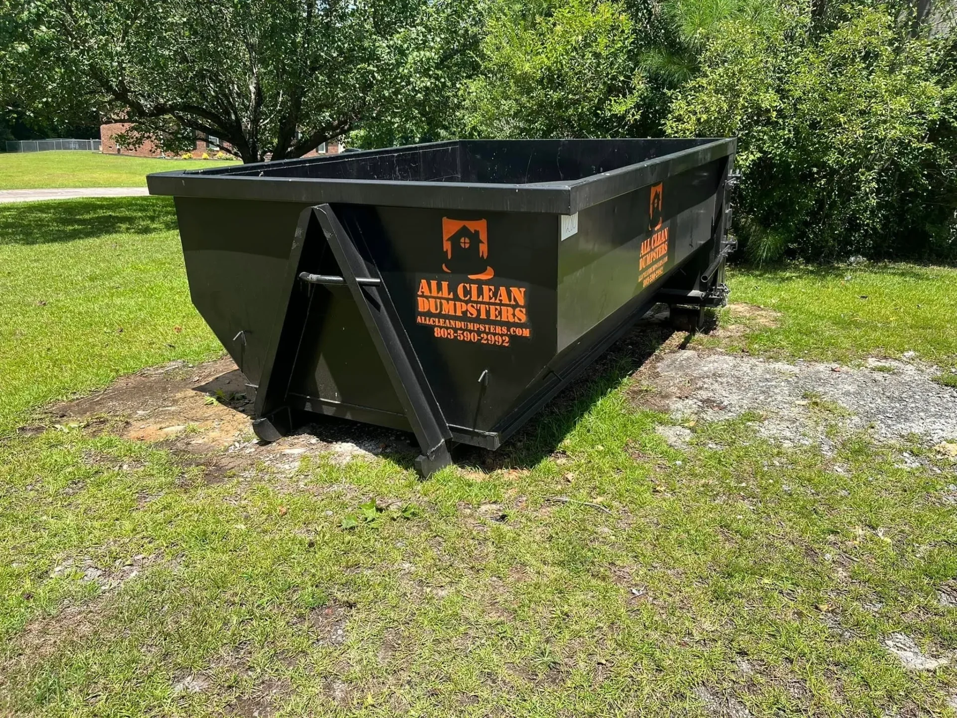 A dumpster sitting in the grass near some trees.